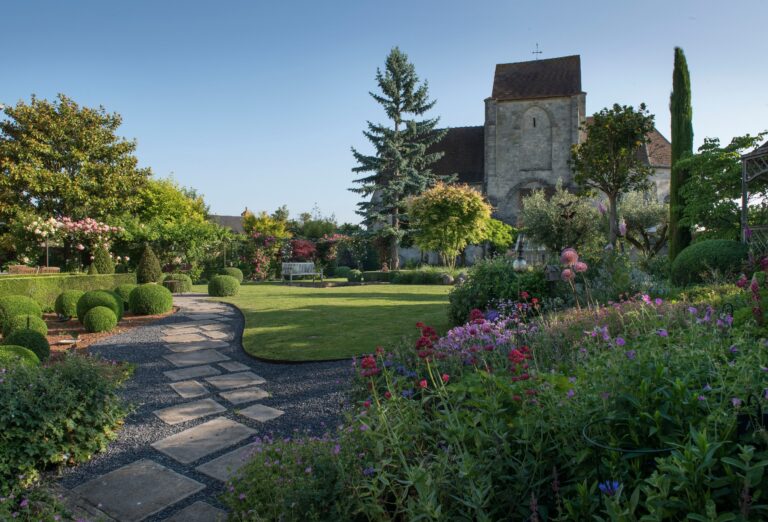 Jardin fleuri en face d'une église avec des buissons taillés en formes rondes er coniques